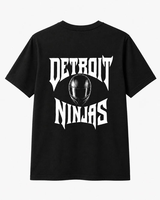 A black short-sleeve t-shirt shown from the back, featuring a large white graphic print that reads 'DETROIT NINJAS' with a black ninja helmet in the center, set against a plain light gray background.